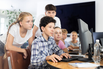 Excited minor male and female students learning computer programs together in informatics classroom