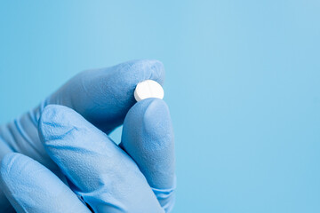 Doctor, pharmacist or scientist hand in glove holding white pill, vitamin or supplement on blue...