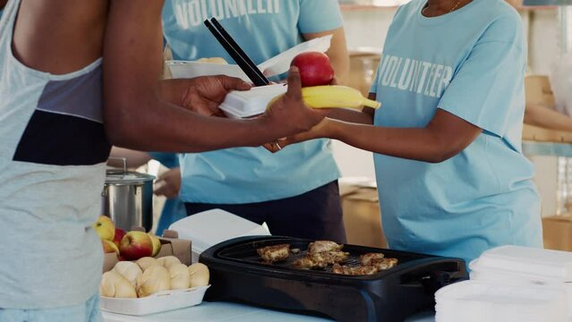 Friendly volunteers distribute generous food donations to homeless people showing impact of charitable works. Close-up of voluntary individuals serving and sharing warm meals to the less fortunate.