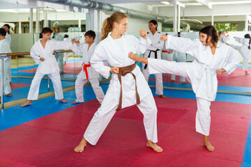 Pair of teenager girls wearing kimono practicing new karate moves during training in gym © JackF