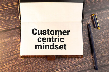 Top view of magnifying glass,pen and notebook written with Customer Centric Mindset on wooden background