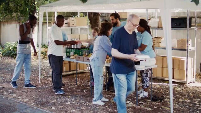 Multiracial volunteers engage in acts of charity by providing warm meals to underprivileged and homeless people. Non-profit group promote supportive atmosphere by extending essential aid to the poor.
