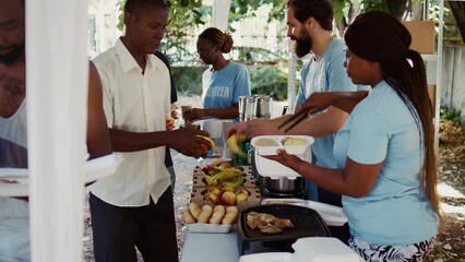 Side-view shot capturing charity workers distributing free food to homeless people and those in need. Humanitarian aid team handing out freshly prepared meals to the less privileged. Handheld shot.
