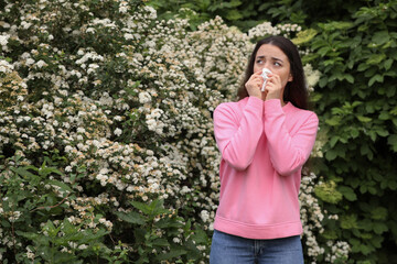 Woman suffering from seasonal pollen allergy near blossoming tree on spring day