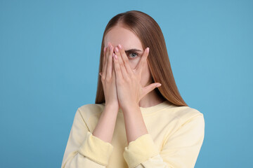 Embarrassed woman covering face with hands on light blue background