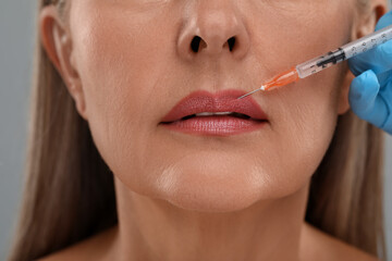 Doctor giving lips injection to senior woman on light grey background, closeup. Cosmetic surgery