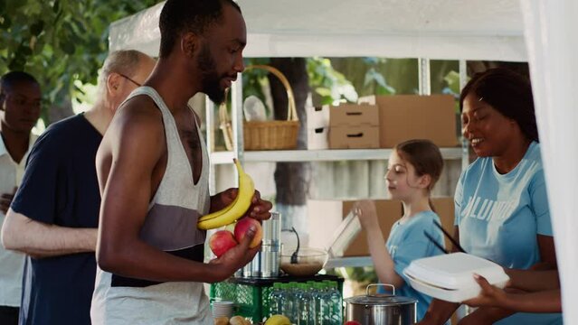 Friendly volunteers offering hunger relief to poor and needy individuals. People of different ethnicities who are less fortunate and homeless are fed by a charitable organization. Tripod shot.