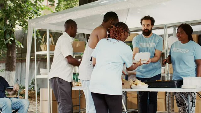 Multicultural non-profit team distributes and delivers humanitarian help to the needy and underprivileged. Black volunteer woman assists african american guy with crutches at food drive. Handheld.