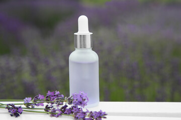 Obraz na płótnie Canvas Bottle of essential oil and lavender flowers on white wooden table in field