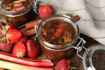 Jars of tasty rhubarb jam, fresh stems and strawberries on wooden table