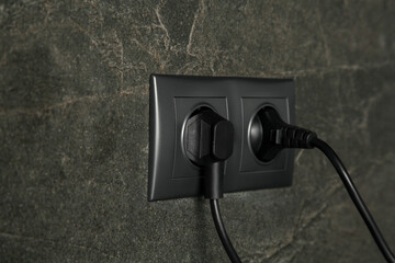 Power sockets with inserted plugs on dark grey wall, closeup. Electrical supply