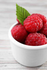 Tasty ripe raspberries and green leaf on white wooden table, closeup