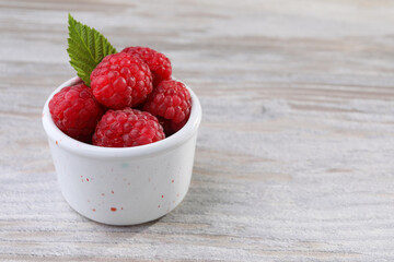 Tasty ripe raspberries and green leaf on white wooden table, space for text