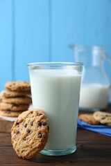 Delicious chocolate chip cookie and glass of milk on wooden table, closeup