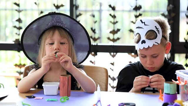 Cute brother and sister in Halloween costumes are doing festive crafts. 