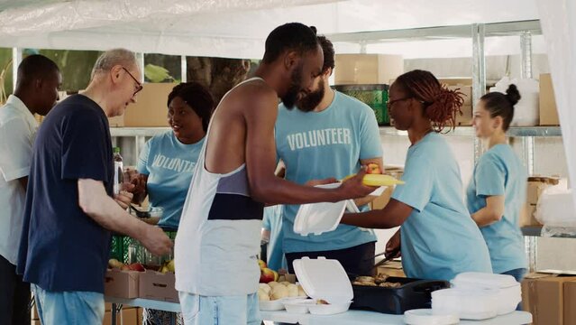Multicultural volunteers distribute free food and essentials to the underprivileged. Voluntary people provide the less fortunate with humanitarian aid and hunger assistance in homeless shelters.