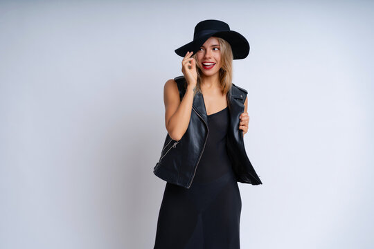 A lovely woman in a black grunge outfit poses against a white background, wearing vibrant makeup and a cheerful expression