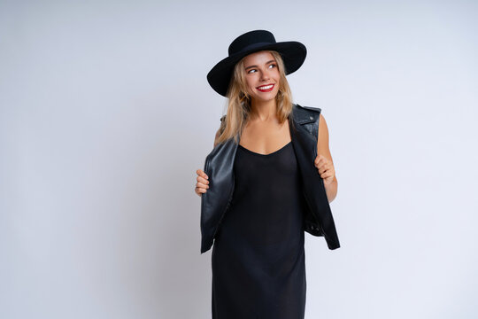 A lovely woman in a black grunge outfit poses against a white background, wearing vibrant makeup and a cheerful expression
