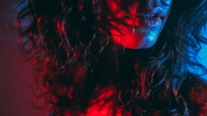 Club lifestyle. Sensual lady. Unrecognizable passionate brunette woman beautiful lips curly shiny hair radiant sweaty face skin in blue red light on dark background. - obrazy, fototapety, plakaty