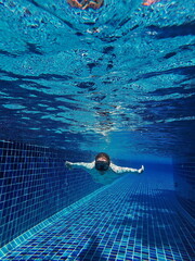A woman in a swimming mask dives underwater in a swimming pool at a tropical resort. The sun's rays break through the water.