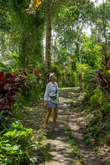 A woman stands on a stone path in a tropical forest. She raised her head and looked at the tree crowns. The sun's rays break through the tree crowns.