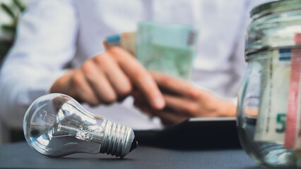 Electric light bulb. Man hands counting expenses on electricity banknotes of euro cash accounting...