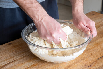 Man's hands kneading dough inside a glass bowl.