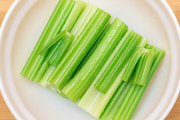 Fresh Chopped Celery Sticks with Water Drops in White Bowl - Top View. Vegan and Vegetarian Culture. Raw Food. Healthy Diet with Negative Calorie Content