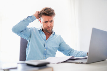 Mental health at work concept. Man scratches his head showing frustration gesture while working at...