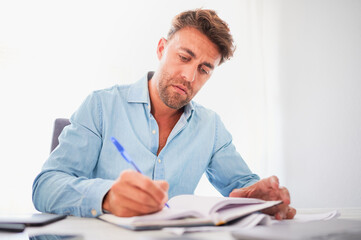 Entrepreneur young man dressed in blue shirt writes on the agenda at his workplace in the office.