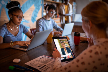 Young and diverse group of flat sharing roommates studying together and asking for advice from their professor via video call in their shared apartment