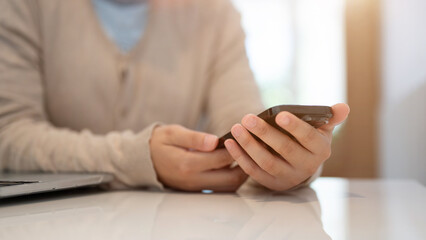 A woman using her smartphone, texting or scrolling on social media while sitting in a cafe.