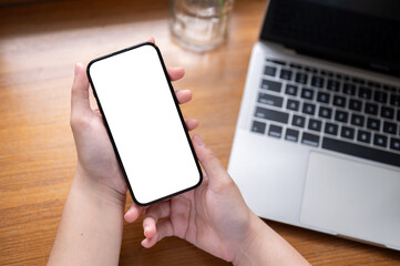 Close-up image of a white-screen smartphone in a woman's hands above a wooden desk with a laptop.