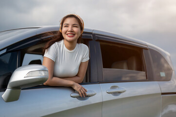 An attractive Asian woman is enjoying the wind outside the car and having fun during her road trip.
