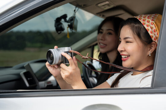 A cheerful Asian girl is taking pictures with her camera during her road trip with friends.