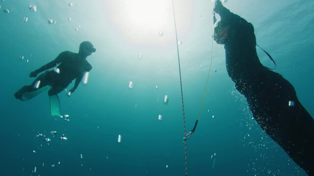 Freediving on the rope in a sea. Male freediver ascends along the rope in monofin and meets buddy leading and securing him till the surface