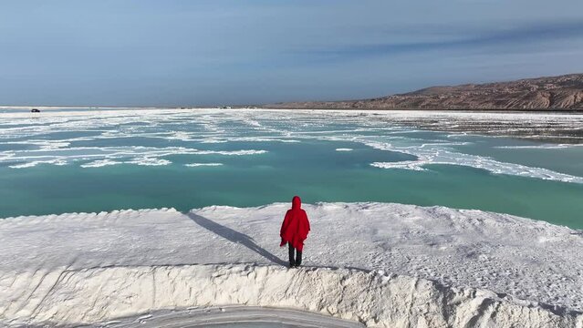 A woman in red dress standing at the Mangya emerald lake in QInghai province, China.