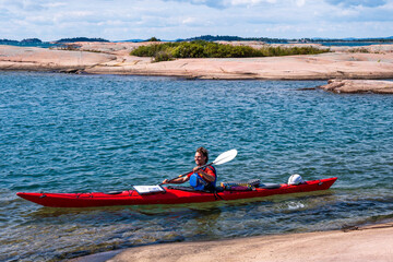 sea kayaking on georgian bay a happy smiling young man paddling a red sea kayak from right to left across the frame on a sunny fall day with smooth red granite rocks in the foreground. room for text