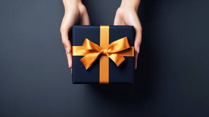 A woman's hands hold a black gift box with an orange bow and ribbons on a black background - Powered by Adobe