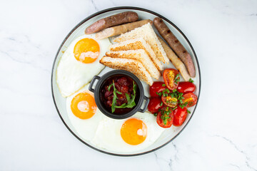 English breakfast with grilled sausages, scrambled eggs, cherry tomatoes and toast