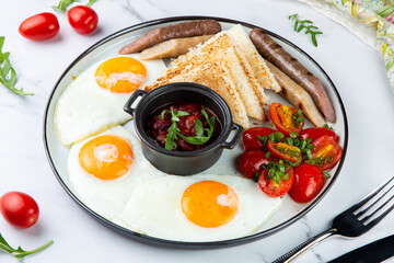 English breakfast with grilled sausages, scrambled eggs, cherry tomatoes and toast