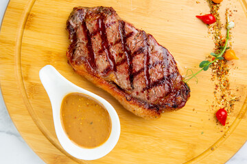 beef steak with spices and sauce on a wooden board on a marble background