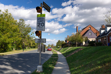 Quiet suburban street in Frederick, MD, with two-story houses, green lawns, and a school zone warning sign flashing at 20 miles per hour, emphasizing the importance of road safety
