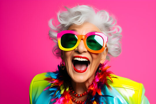 Happy senior retired woman in colourful neon clothes, isolated on pink background