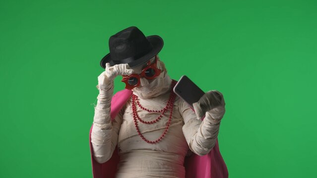 Green screen isolated chroma key photo capturing a mummy wearing pink jacket, hat and accessiores taking selfies, pictures of itself on a smartphone.