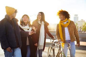 Group of happy multiracial friends laughing together while walking around city harbour on a sunny winter day.