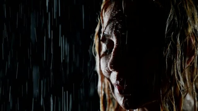 beautiful female face in rain in night, closeup view, woman standing under water flows
