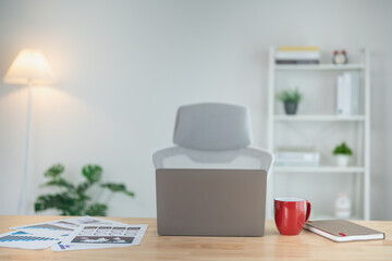 Close up view of worktable workpalce with laptop, chart documents, red cup of coffee, notebook, and decoration in home office room. Work at home place in the living room concept.