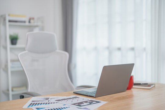 Close up view of worktable workpalce with laptop, chart documents, red cup of coffee, notebook, and decoration in home office room. Work at home place in the living room concept.