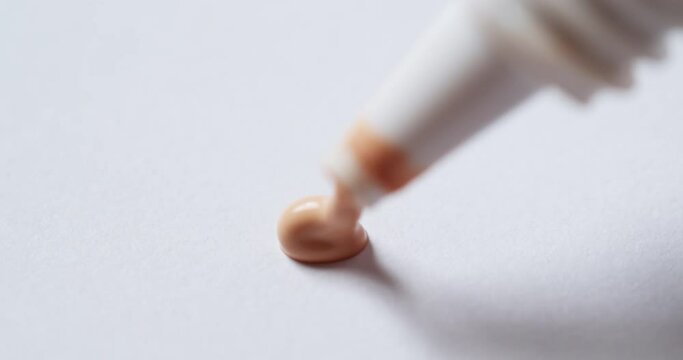 Squeezing a pea-size waterproof nude liquid concealer from a plastic tube onto a clean, white palette board.
